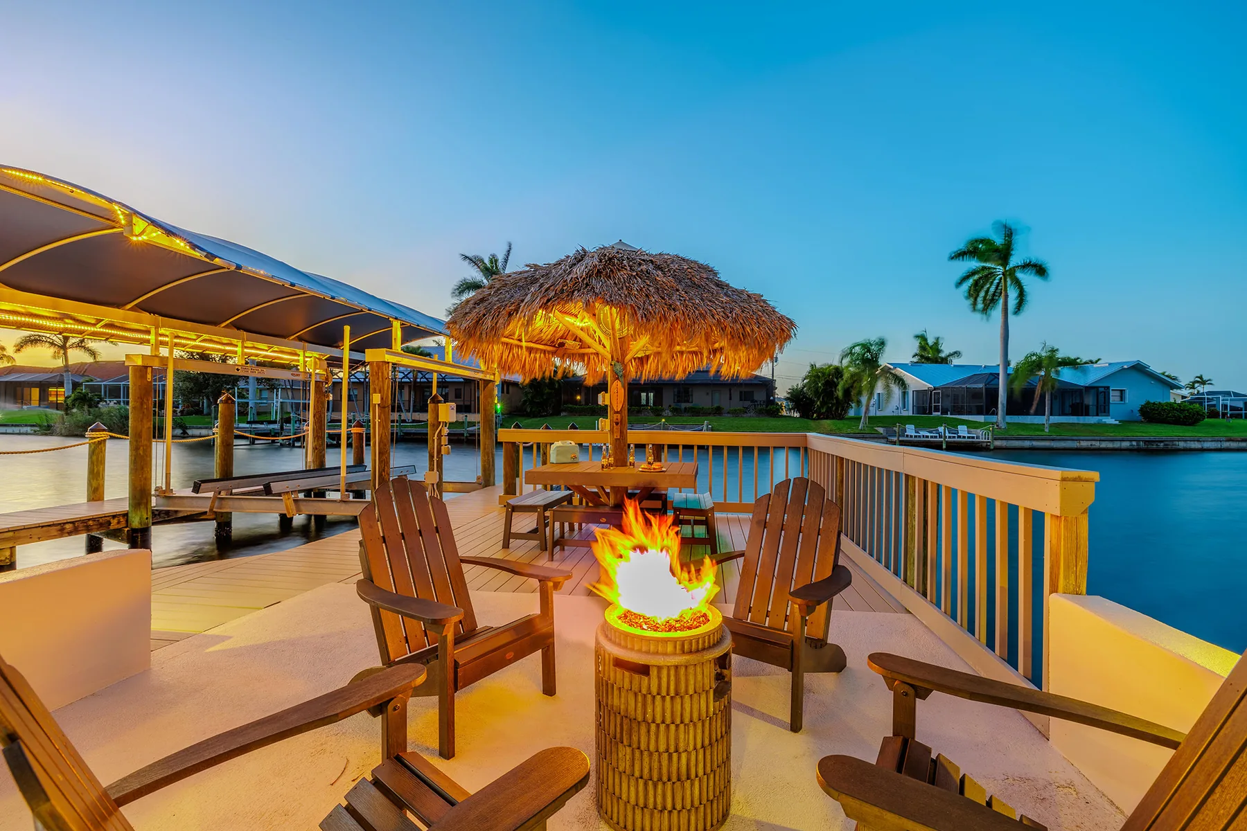 Canal-front dock deck with tiki hut, fire pit and chairs at dusk
